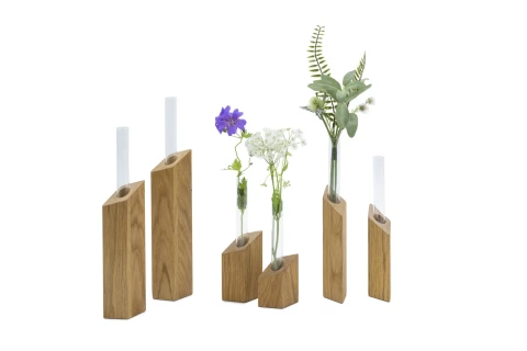 F&uuml;nf unterschiedlich hohe, rechteckige Holzvasen mit schr&auml;gem oberen Rand, jeweils mit einem schmalen Glasbeh&auml;lter. Die Glasbeh&auml;lter enthalten diverse Pflanzen: eine blaue Bl&uuml;te, kleine wei&szlig;e Bl&uuml;ten, gr&uuml;ne Farnbl&auml;tter und Zweige. Anordnung der Vasen von links nach rechts auf wei&szlig;em Hintergrund.