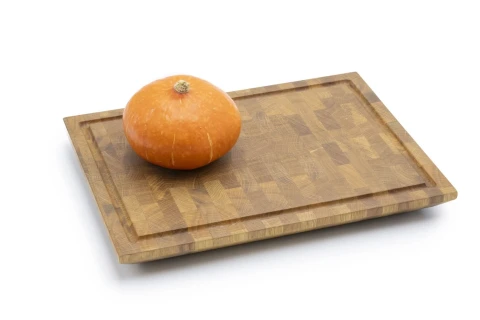Kleiner runder orangefarbener K&uuml;rbis mit heller Stielnarbe liegt zentriert auf einem rechteckigen Holzschneidebrett mit matt gemusterter Oberfl&auml;che und leicht erh&ouml;htem Rand.