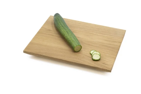 Gr&uuml;ne, ungeschnittene Gurke auf einem hellbraunen Holzschneidebrett, neben der Gurke drei d&uuml;nne Gurkenscheiben. Schneidebrett liegt auf einer wei&szlig;en Fl&auml;che.