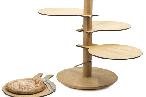 Holzgestell mit vier runden, versetzt angeordneten Etagen, die an einem zentralen Standfu&szlig; befestigt sind. Daneben ein rundes Holzbrett mit einer gebackenen Pizza, auf dem Brett liegen ein Messer und eine Gabel.