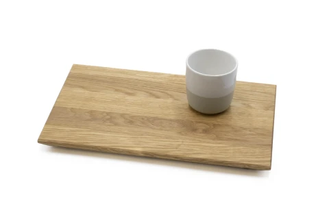 Wei&szlig;e Tasse mit grauer unterer H&auml;lfte auf rechteckigem Schneidebrett aus hellbraunem Holz mit sichtbarer Maserung, auf wei&szlig;em Hintergrund.