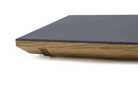 Schwarze rechteckige Platte mit glatter, matter Oberfl&auml;che, montiert auf einer schr&auml;gen, holzfarbenen Basis aus nat&uuml;rlichem Material mit sichtbarer Maserung. Am &Uuml;bergang zwischen Platte und Basis ist ein filigranes, dunkleres Verbindungselement angebracht.