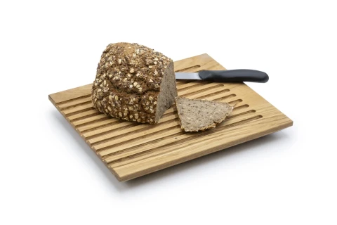 Vollkornbrotlaib mit Haferflockenkruste auf einem gestreiften Holzbrett, daneben ein abgeschnittenes Brotscheibenst&uuml;ck und ein schwarzes Brotmesser mit gl&auml;nzender Klinge.