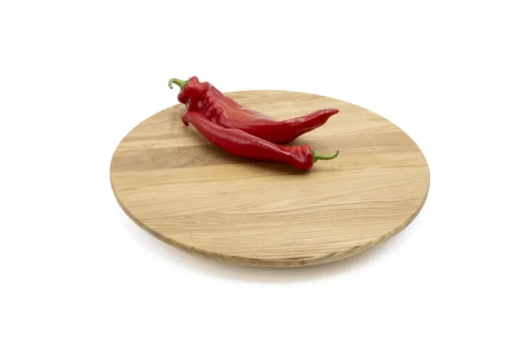 Zwei rote Chilischoten mit gr&uuml;nen Stielen liegen auf einem runden, hellbraunen Holzbrett, das auf einer wei&szlig;en Fl&auml;che platziert ist.